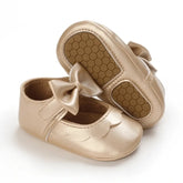 Sapato para bebê menina dourado, com laço delicado e sola macia antiderrapante, exibido em fundo branco para destaque do produto.
