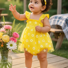 Bebê menina em pé, sorrindo, usando body amarelo com tule estampado de margaridas e faixa de cabelo combinando, em cenário ao ar livre