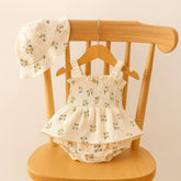 "Conjunto infantil feminino com body floral branco de alças e chapéu combinando, exibido em cabide de madeira em cadeira clara — Baby Hello."