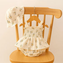 "Conjunto infantil feminino com body floral branco de alças e chapéu combinando, exibido em cabide de madeira em cadeira clara — Baby Hello."