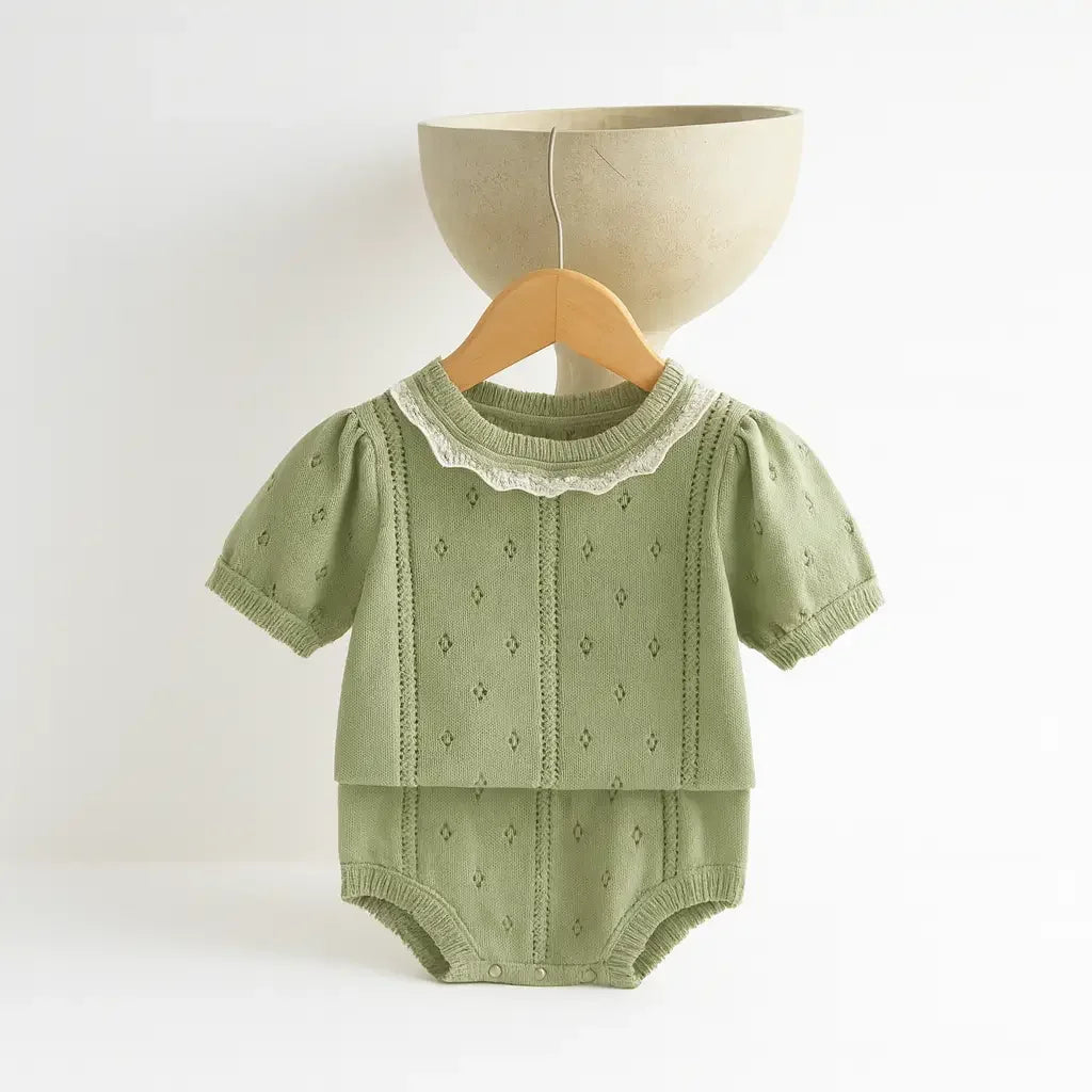 romper unissex em tricô de algodão verde com detalhes bege, manga curta e gola rendada, ideal para bebê recém-nascido, pendurado em cabide no fundo branco.