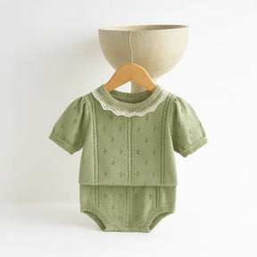 romper unissex em tricô de algodão verde com detalhes bege, manga curta e gola rendada, ideal para bebê recém-nascido, pendurado em cabide no fundo branco.