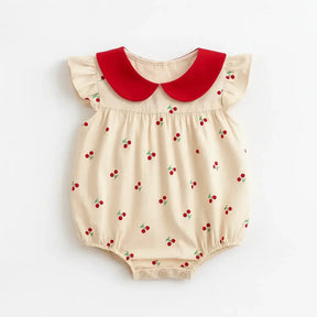 Body infantil feminino bege com estampa de cerejinhas vermelhas, gola peter pan vermelha e mangas curtas com babados.