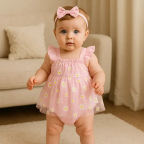 Bebê menina de aproximadamente 8 meses em pé, usando body rosa com saia de tule estampada de margaridas e faixa de cabelo combinando, em cenário aconchegante com sofá e cortina ao fundo.