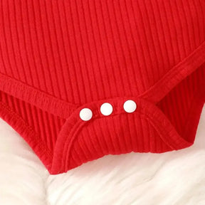 Conjunto infantil feminino composto por body vermelho canelado de manga longa com babadinhos nos ombros e jardineira xadrez vermelha com alças e aplique de rena com laço. A peça está disposta sobre fundo branco, com destaque para o visual natalino e delicado.