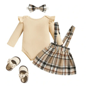 Conjunto infantil feminino com body bege de manga longa, saia xadrez com detalhe de ursinho e laço, faixa de cabelo combinando e sapatinhos bege