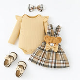 Conjunto infantil feminino com body bege de manga longa, saia xadrez com detalhe de ursinho e laço, faixa de cabelo combinando e sapatinhos bege