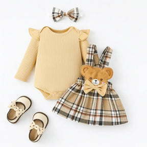 Conjunto infantil feminino com body bege de manga longa, saia xadrez com detalhe de ursinho e laço, faixa de cabelo combinando e sapatinhos bege