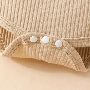 Detalhe do body infantil bege canelado com fechamento de botões de pressão na parte inferior.