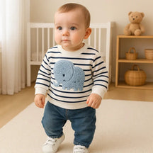 Bebê em pé vestindo o conjunto infantil masculino com blusa listrada e estampa de elefante azul, calça jeans e tênis branco, em ambiente acolhedor.