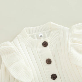Detalhe do macacão bebê menina branco de tricô, mostrando botões frontais escuros e babados delicados nos ombros.