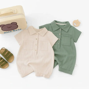 Macacão bebê manga curta em algodão, cores bege e verde, com botões frontais e bolso, acompanhado de sandália e acessórios.