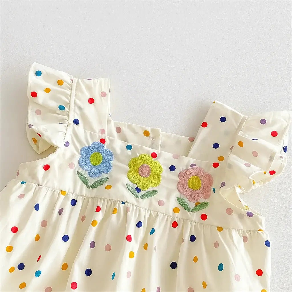 Detalhe do romper infantil feminino com flores bordadas em azul, amarelo e rosa, estampa poá multicolorida e tecido leve.