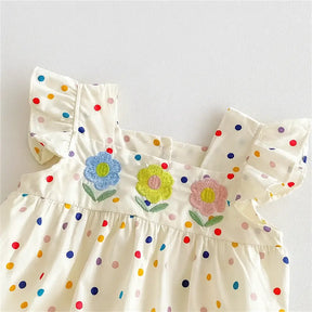 Detalhe do romper infantil feminino com flores bordadas em azul, amarelo e rosa, estampa poá multicolorida e tecido leve.
