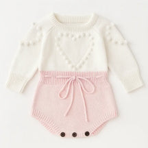 Romper tricot bebê menina rosa e branco com coração em relevo, manga longa, detalhe em pompons e botões na parte inferior.