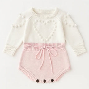 Romper tricot bebê menina rosa e branco com coração em relevo, manga longa, detalhe em pompons e botões na parte inferior.