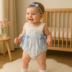 bebê sorrindo usando body floral azul com renda e laços, faixa azul na cabeça e meias rendadas, em quarto infantil iluminado – moda bebê Baby Hello